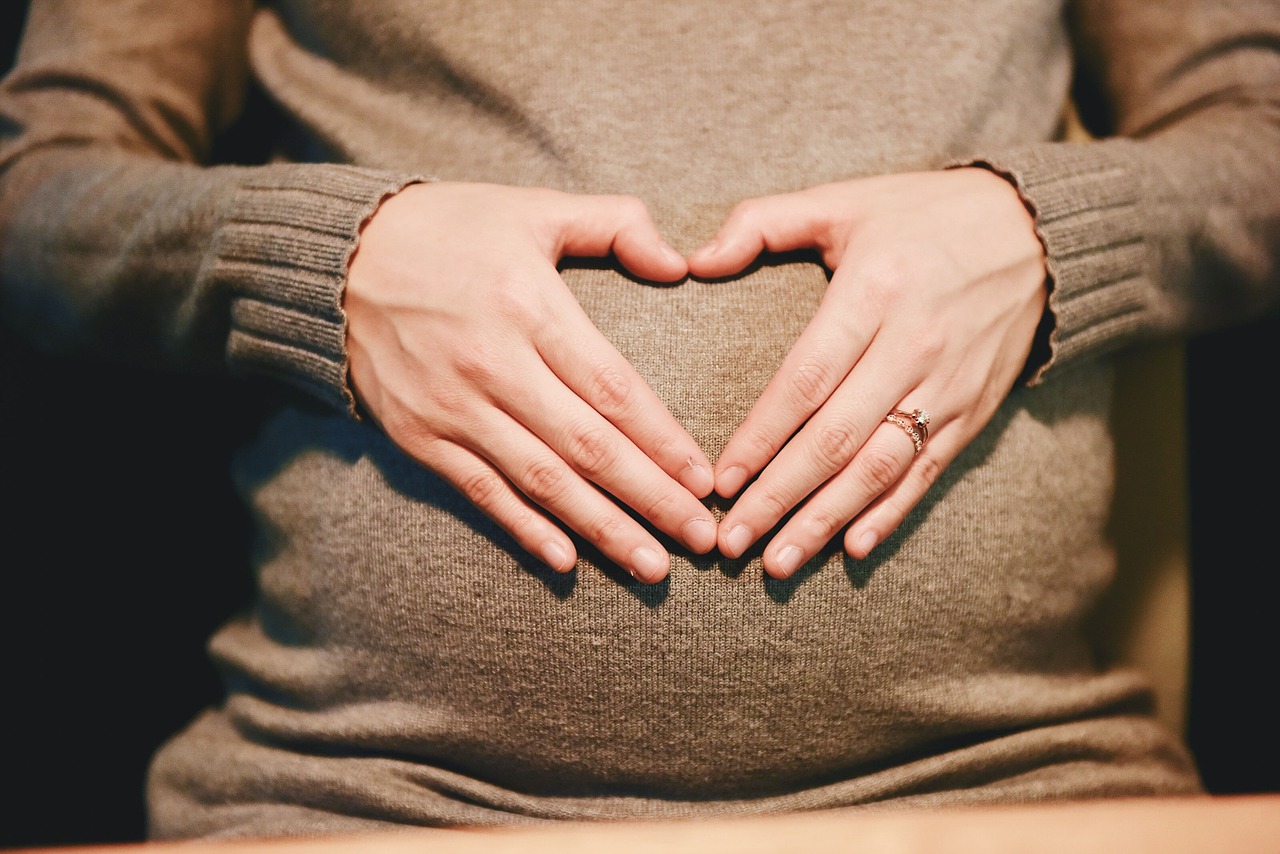 Pregnant woman using hands to make heart over belly